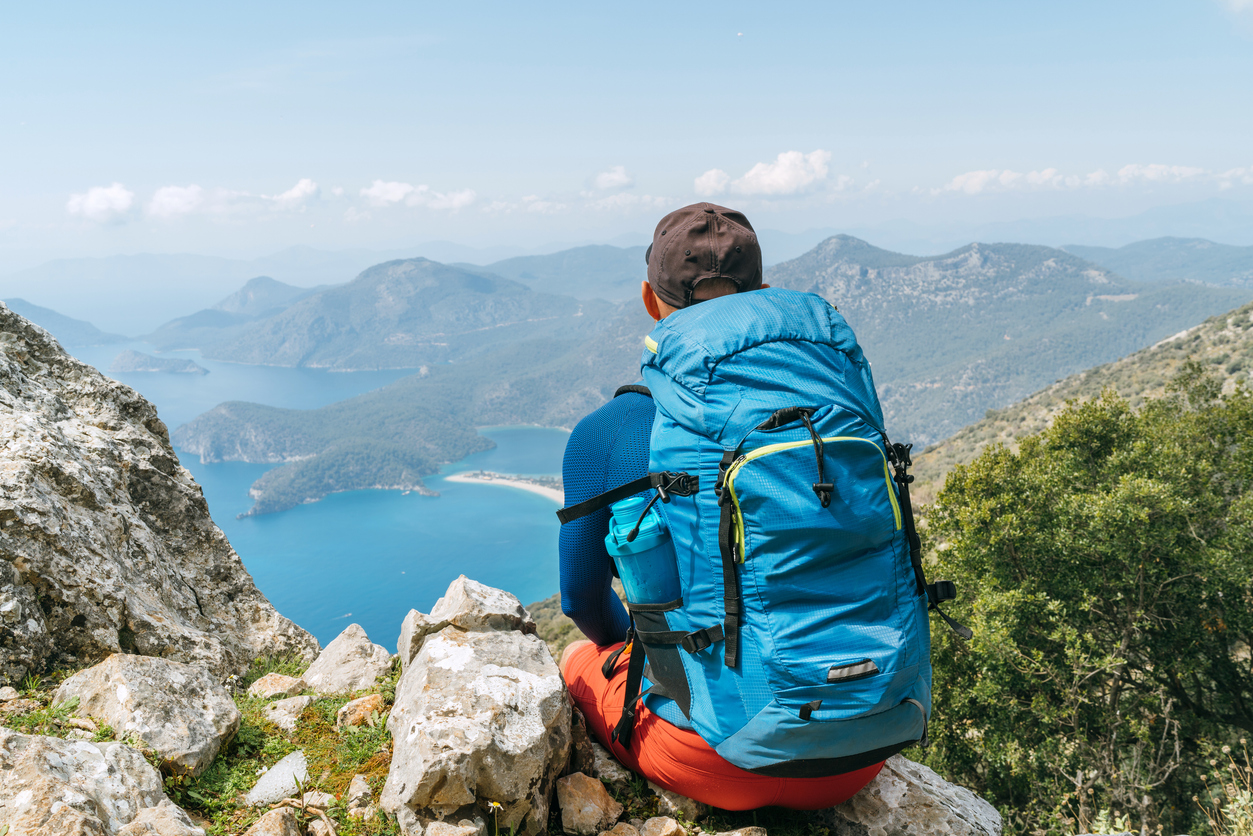 Backpacker-man-sitting-on-clifftop-and-enjoying-the-Mediterranean-Sea-Oludeniz-town-Bay-during-Lycian-Way-trekking-walk