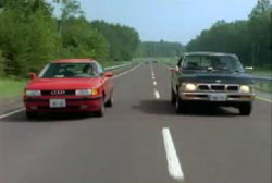 A red compact car and a dark green pick up truck driving down the road next to each other.